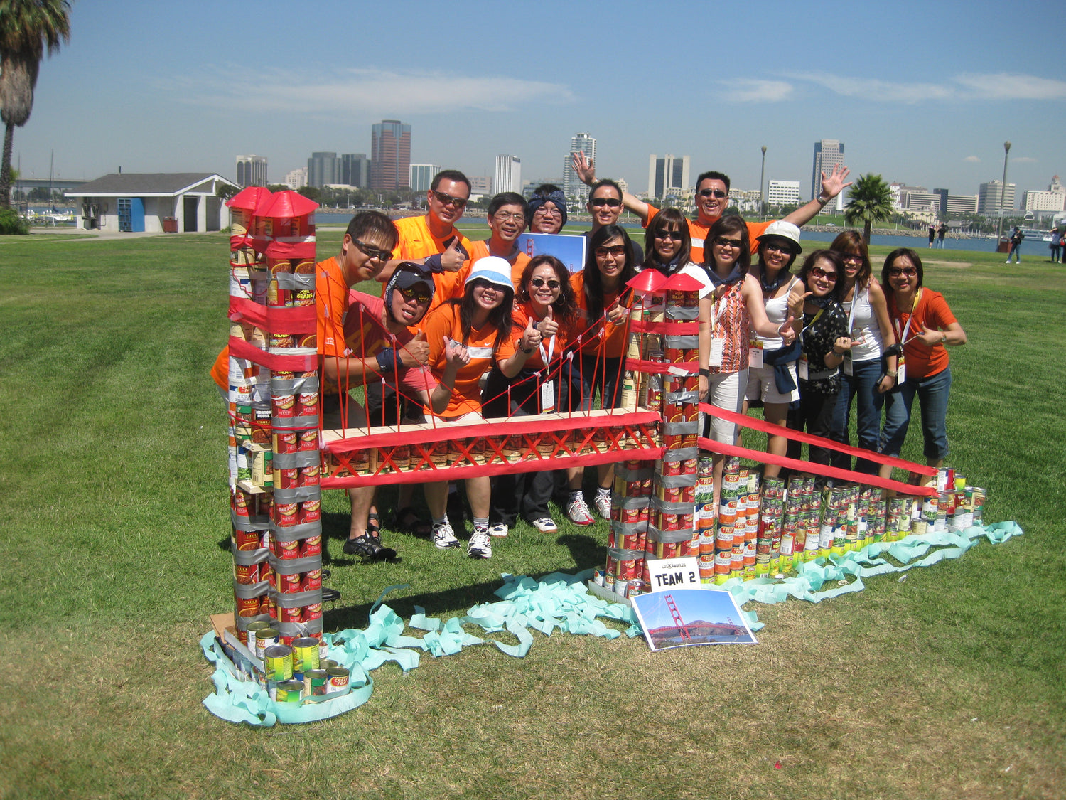 un grupo de personas detrás de un puente hecho con latas y un cartel que dice equipo 2